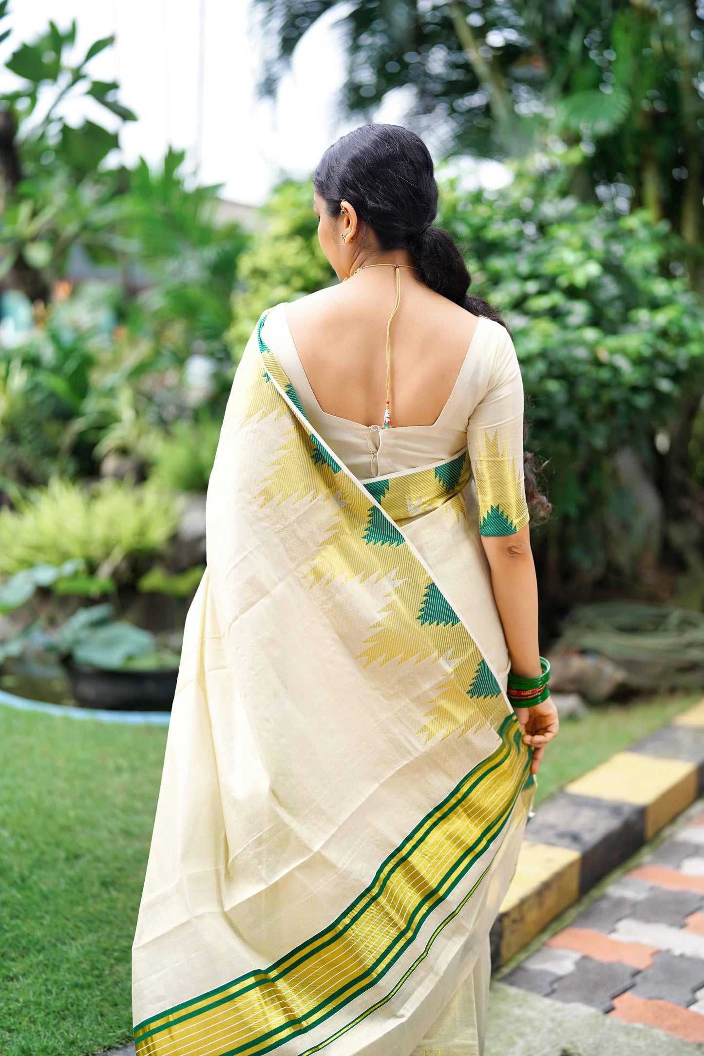 Woman in a Golden Tissue Saree with Green Temple Motifs standing in a garden.