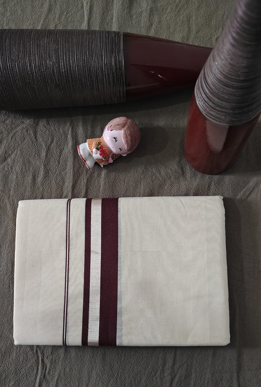 Folded white towel with brown stripes on a bed with a bottle and pink item in the background