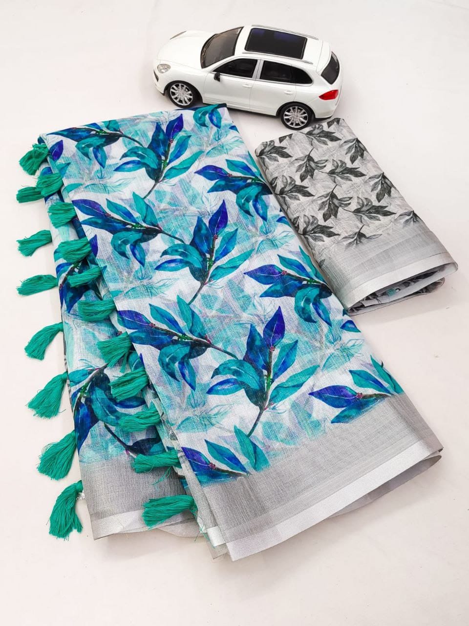 Two folded saree with leaf patterns and tassels on a white background