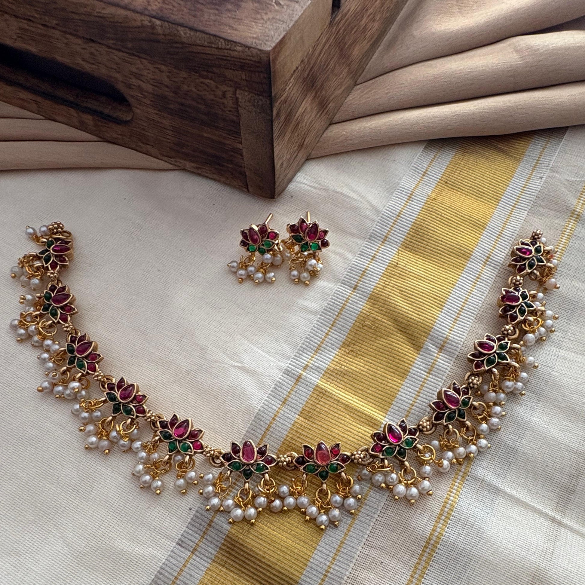 Necklace and earrings set on a saree fabric with a wooden box in the background